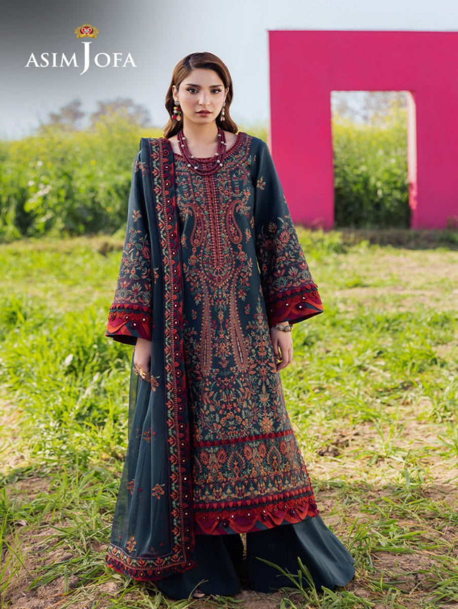 Woman wearing a traditional embroidered outfit in a grassy field with a pink structure in the background, featuring the Asim Jofa brand.