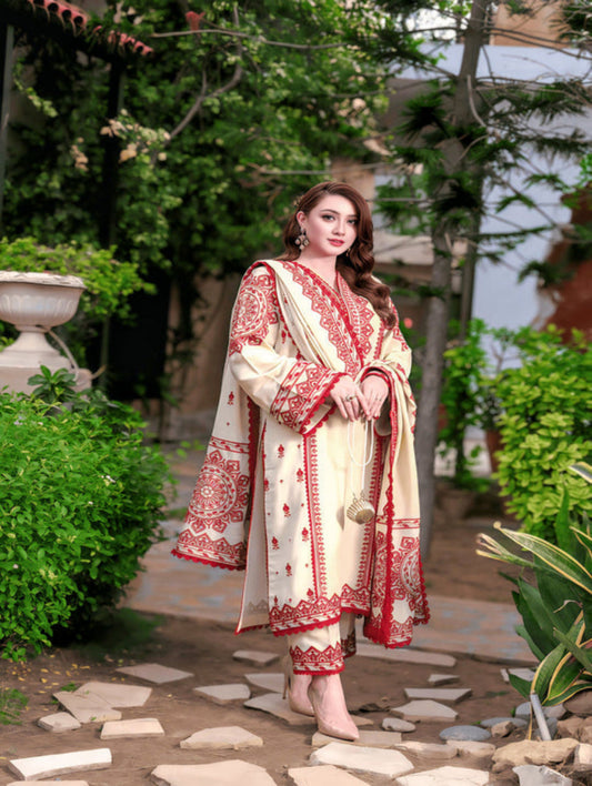 Woman in a red and white traditional outfit standing outdoors with greenery around.