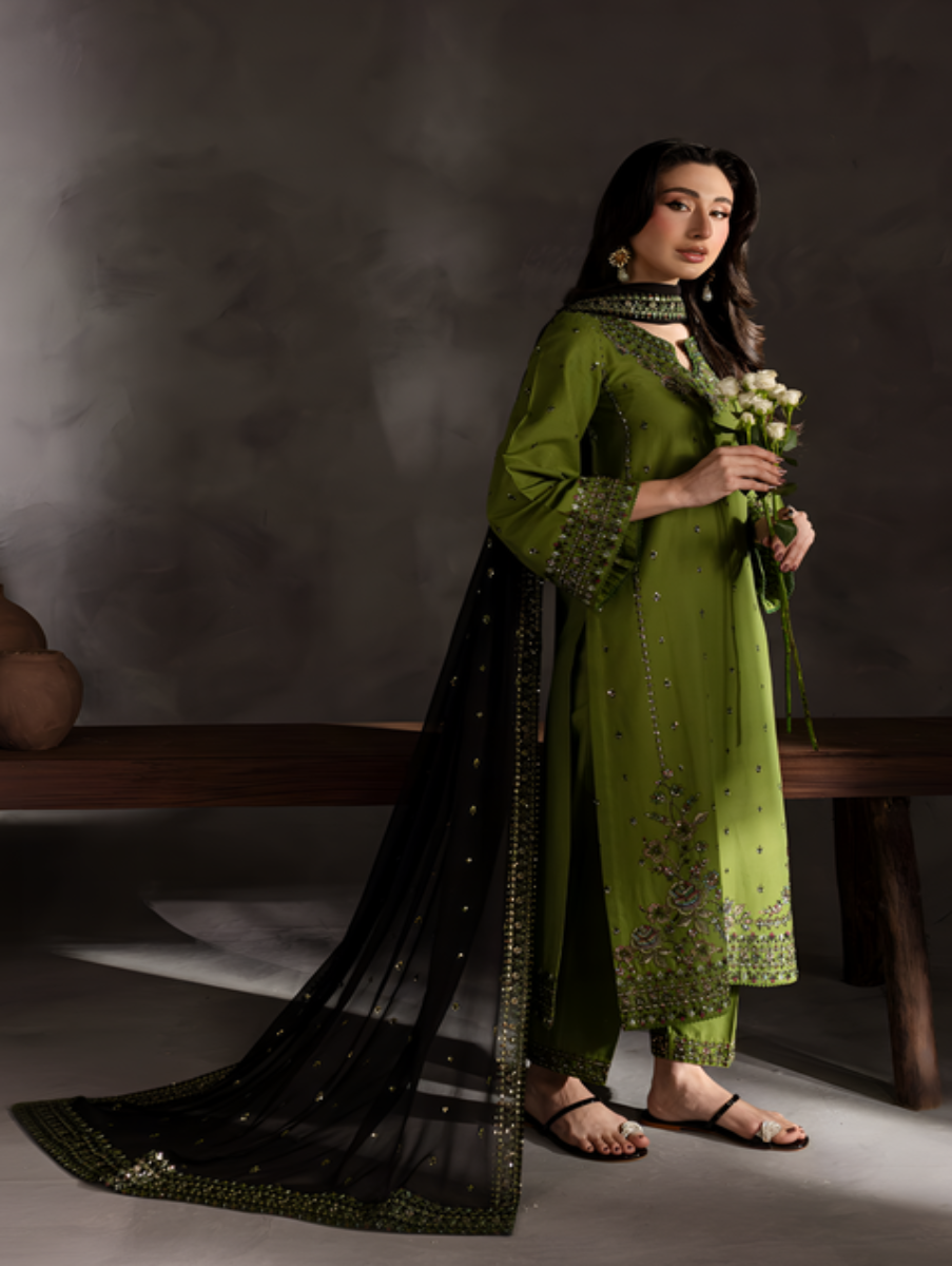 Woman in a green traditional outfit holding flowers against a dark background