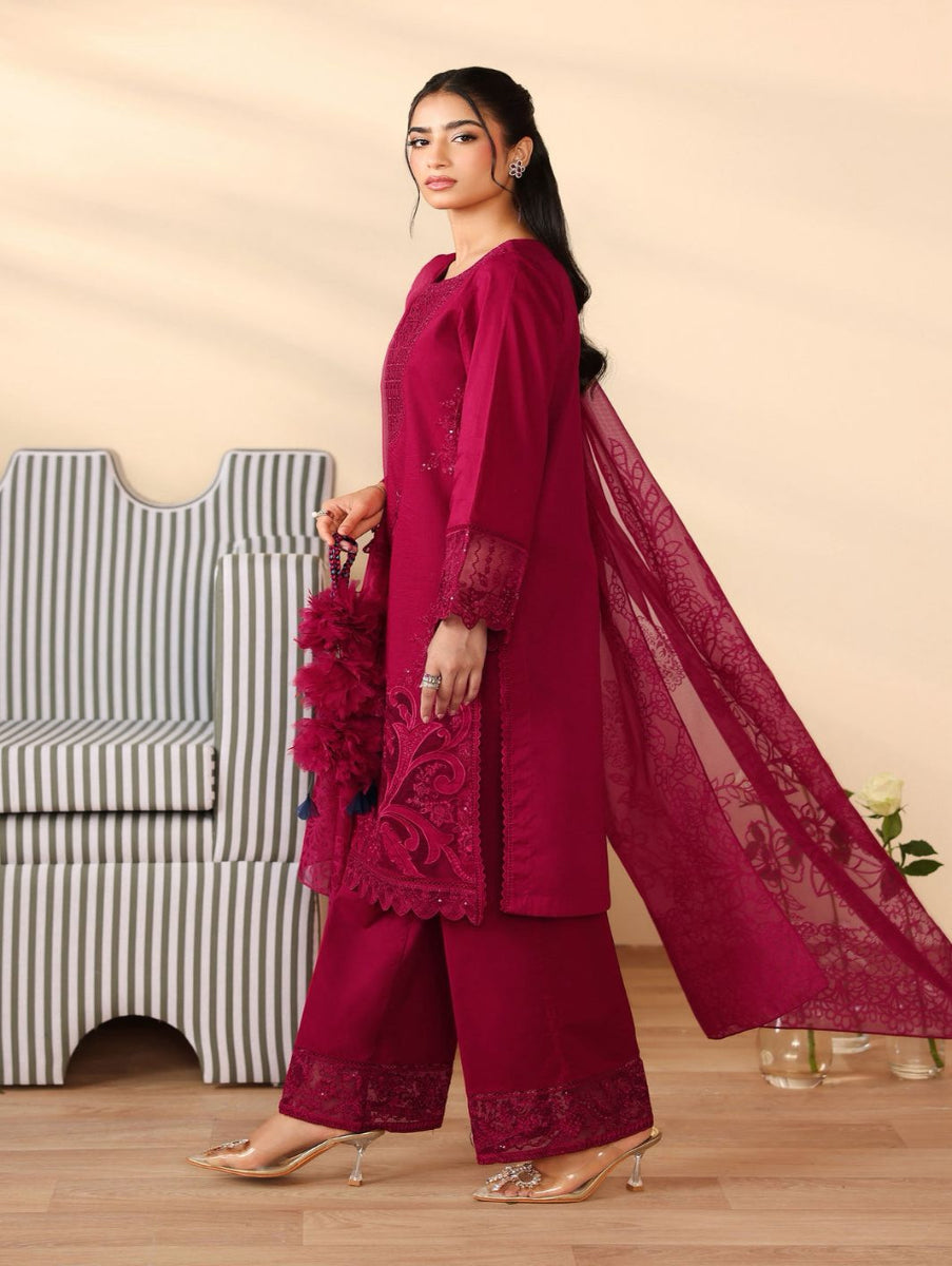 Woman in a magenta traditional outfit with a sheer dupatta, standing against a beige background.