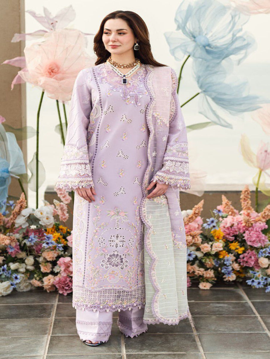 Woman in a light purple embroidered outfit standing in front of floral decorations.